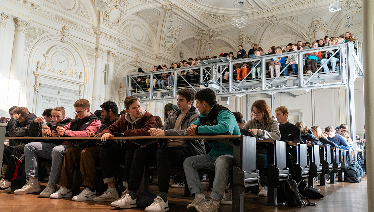 Bei der Begrüssungsrede sind die Bänke der Aula gut gefüllt.