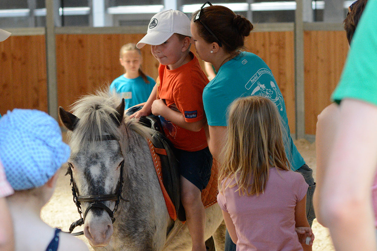 Eine Pferdepflegerin hilft einem Jungen aufs Pony
