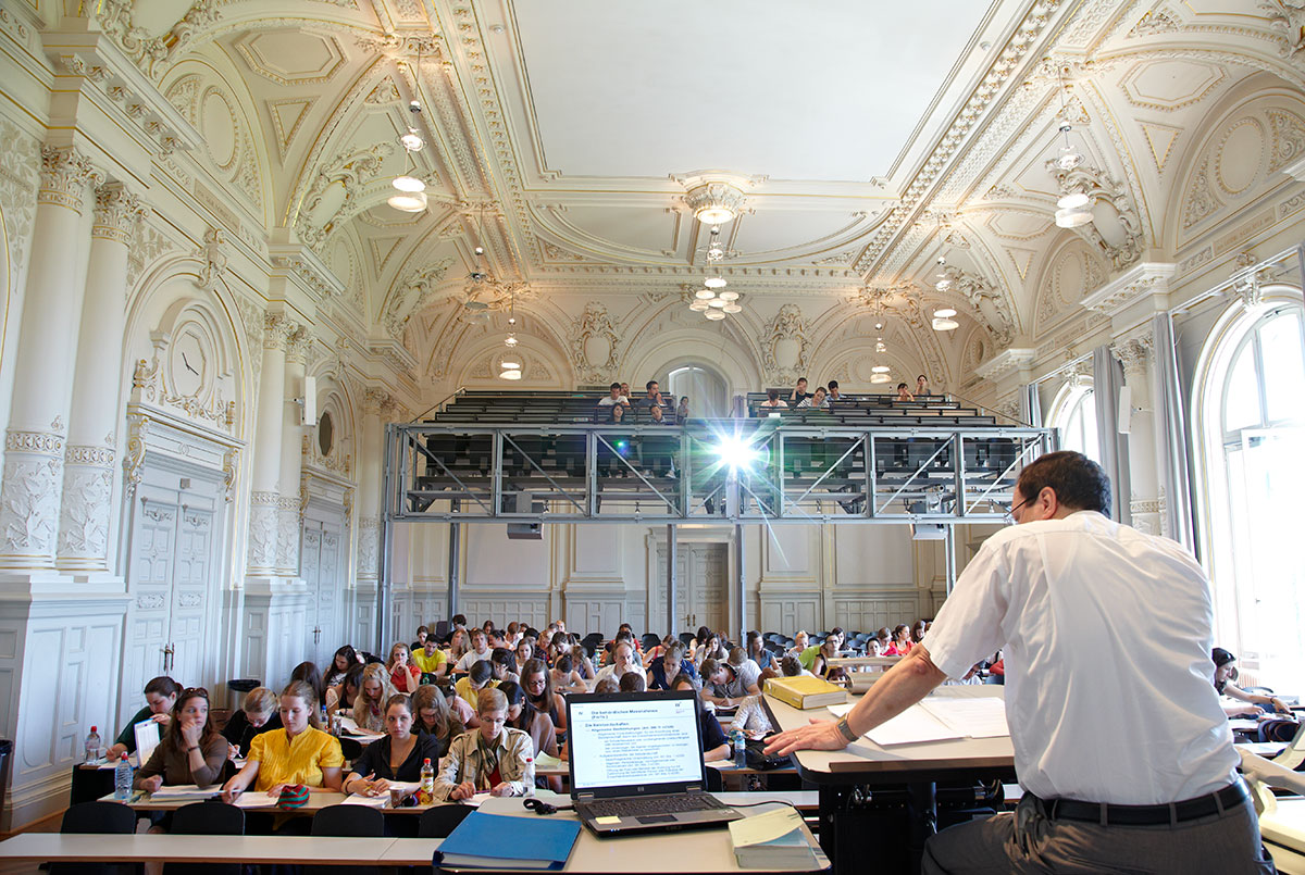 Bild der Aula während einer Vorlesung; der Dozent unterrichtet die Studenten und Studentinnen.