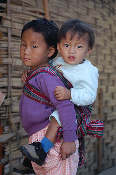 Schwester trägt Bruder auf dem Rücken in Bhutan