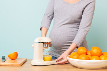 Schwangere Frau presst Saft aus frischen Orangen