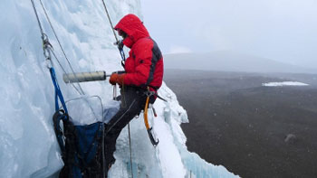 Forscher bohrt an einer Eiswand, im Seil hängend